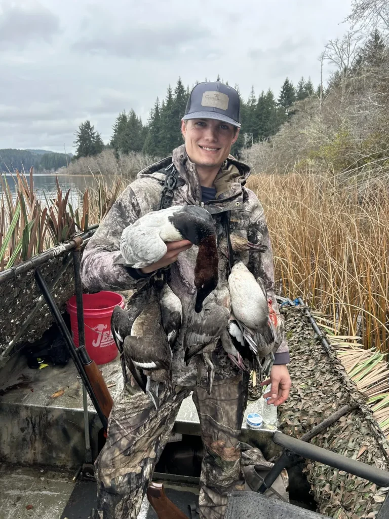 Hunter holding a pair of diver ducks in a boat along the reeds